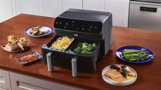 A dual basket air fryer sat on a countertop surrounded by food