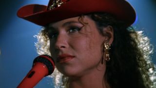 Minnie Driver performing in front of a microphone wearing a cowboy hat in Goldeneye.
