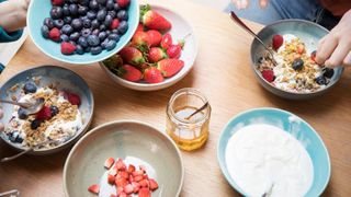 Bowls of strawberries and other berries together on the breakfast table with honey and granola