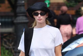 Jennifer Lawrence walking in NYC wearing a white T-shirt, black hat, red pants, a black bag, and red jelly sandals from The Row.