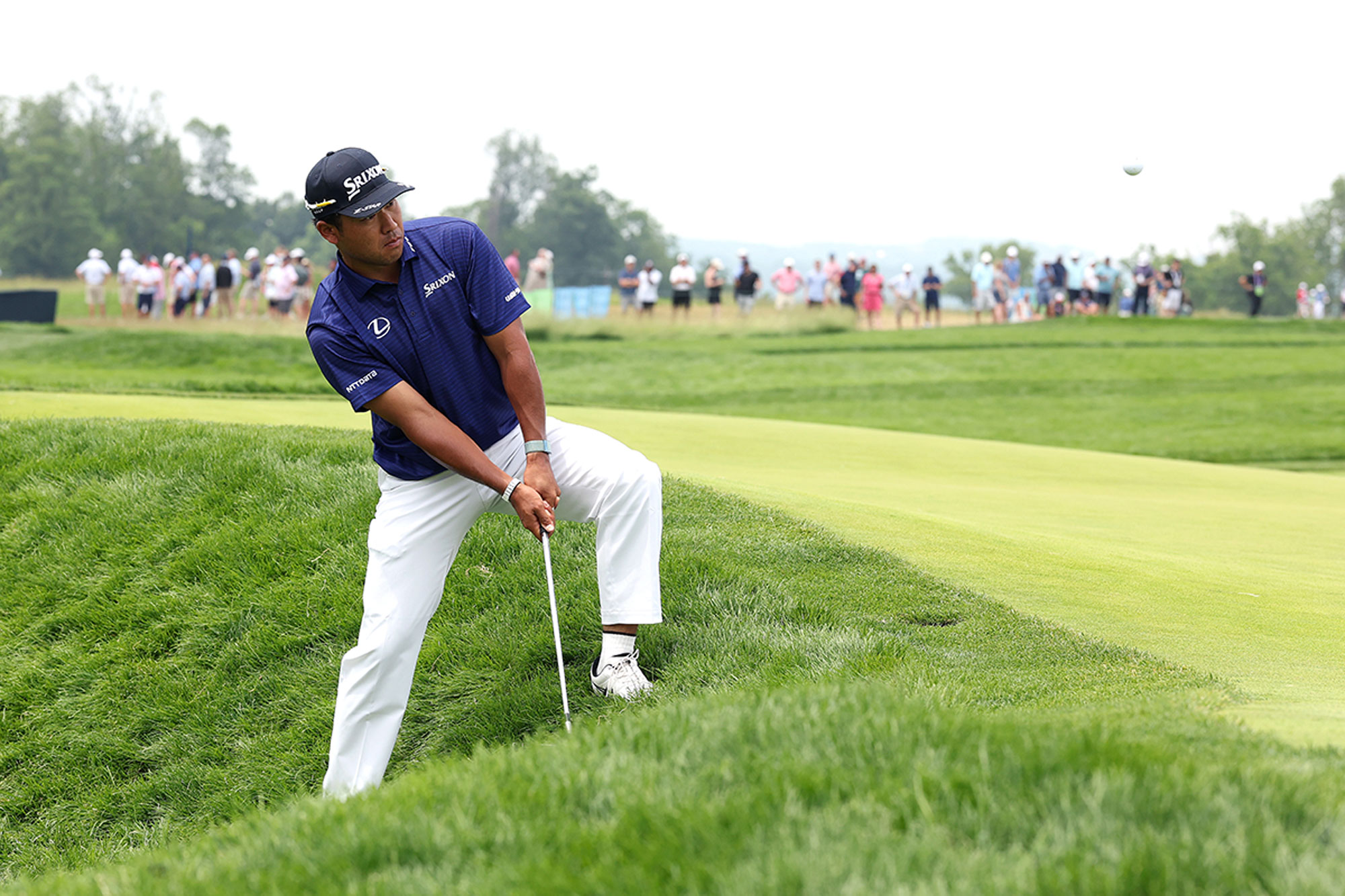 Hideki Matsuyama hitting a very tough shot from long rough, with his feet spread wide open and one leg higher than the other, at Oakmont Country Club for the US Open