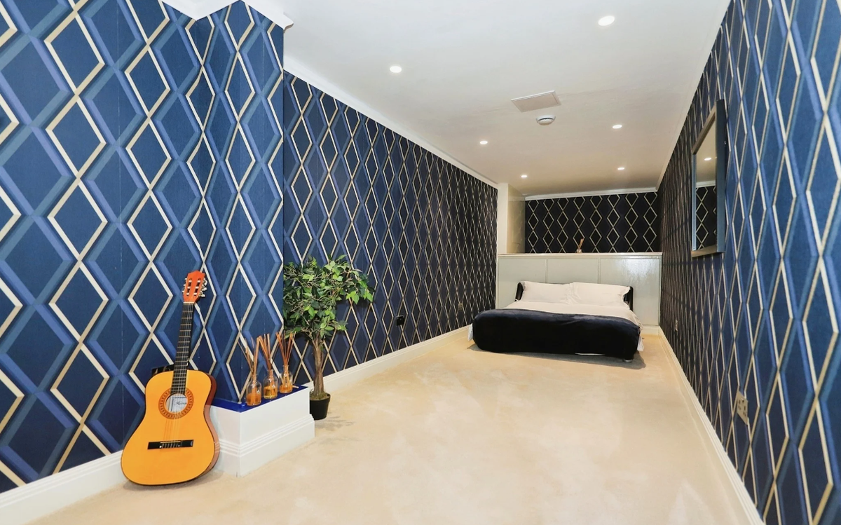 A narrow bedroom with blue patterned wallpaper and white ceramic floor
