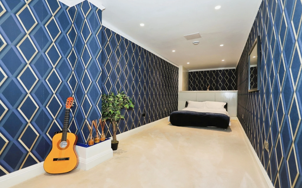 A narrow bedroom with blue patterned wallpaper and white ceramic floor