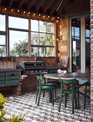 outdoor kitchen with barbecue and tiled floor green chairs