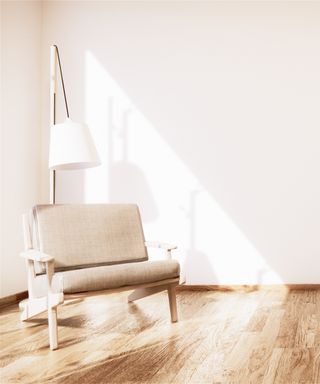 An image of a living room with real wood floors and a beige arm chair and white reading lamp