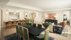 Large, open-plan kitchen, dining room and living space with white walls, bright lighting, green velvet chairs, a breakfast bar, and three sofas.
