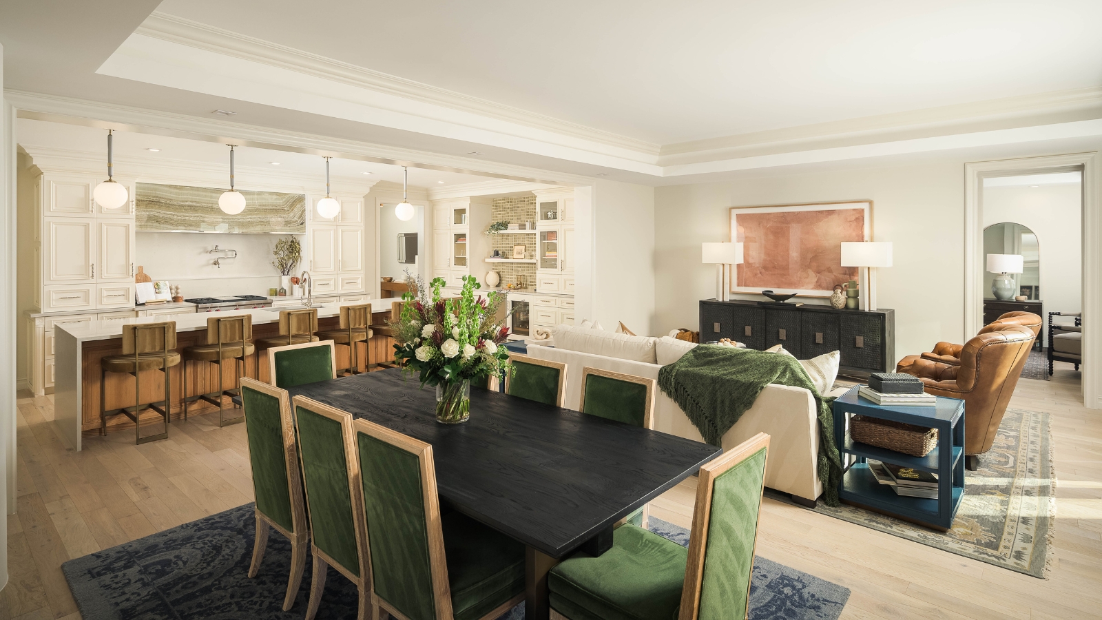 Large, open-plan kitchen, dining room and living space with white walls, bright lighting, green velvet chairs, a breakfast bar, and three sofas.