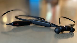 The Beats Flex earbuds in black pictured on a shiny grey surface