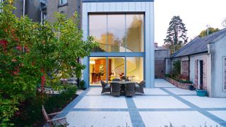 a modern glass box side extension with a large paved patio and a six-person dining table outside