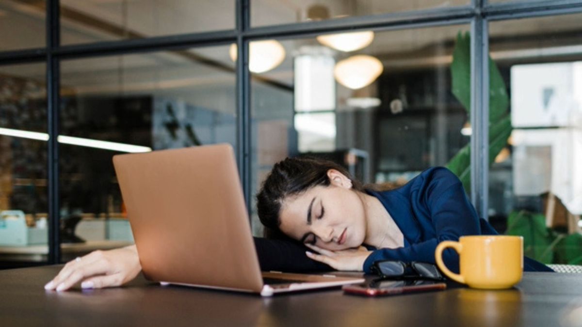 A woman asleep at desk in front of laptop and yellow mug as she&#039;s tired all the time