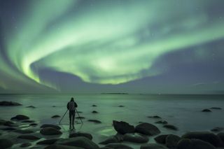 Photographer with tripod with seascape and Northern Lights