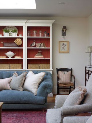 living room with blue sofa and grey armchair with red paneled white display shelving