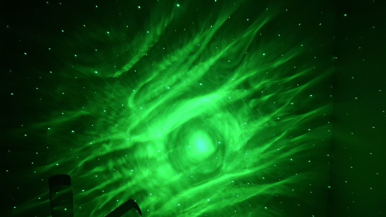 A green projection with dots representing stars is on a wall in a dark room.