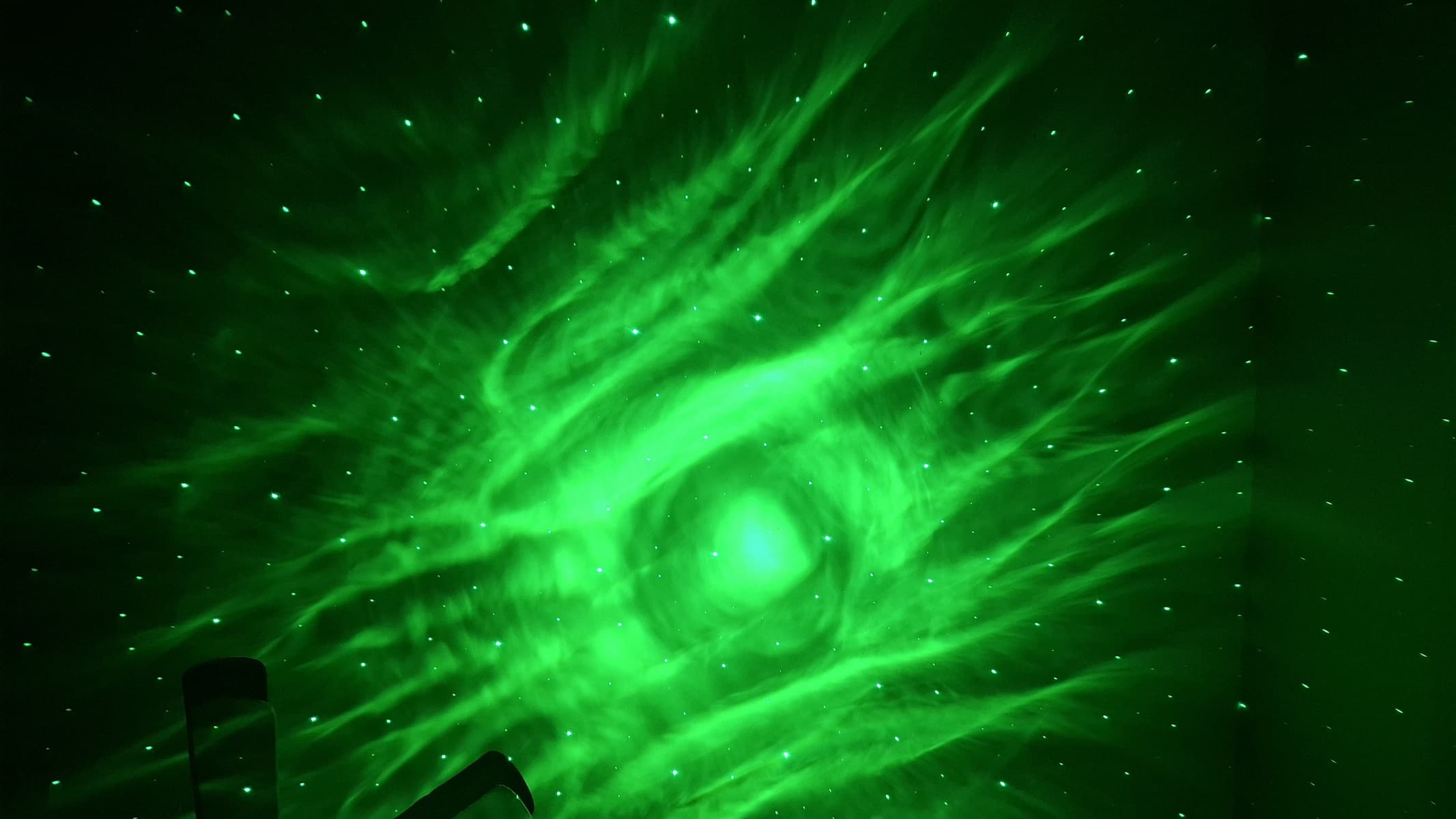 يوجد إسقاط أخضر به نقاط تمثل النجوم على الحائط في غرفة مظلمة.