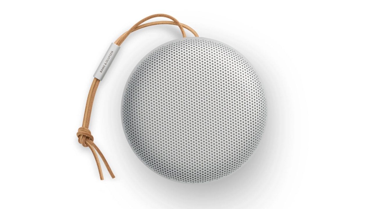 A top-down shot of a silver Bang &amp; Olufsen Beosound A1 (2nd Gen) speaker. It is round and there is a strap attached at the top edge. The background is white.