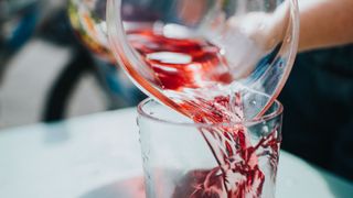 Carafe of red juice being poured into glass on table
