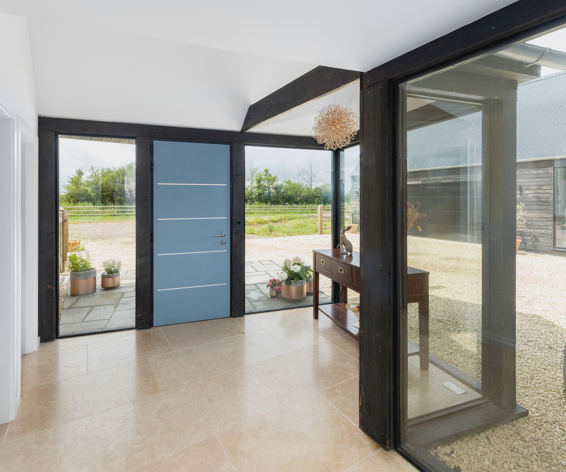 self-build home with modern glazed hallway featuring a contemporary blue front door and neutral-coloured floor tiles