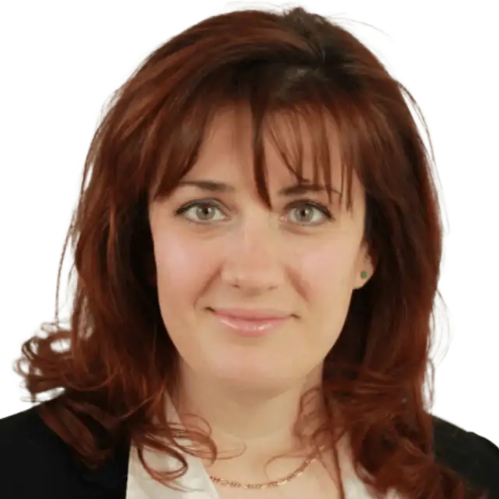 Smiling woman with wavy auburn hair and green eyes, wearing a black blazer over a white top.