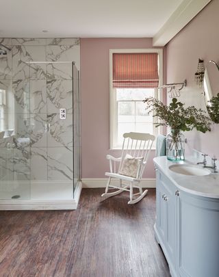 bathroom with blue vanity unit and marble tiles in shower with rocking chair in front of Georgian sash windows and dark wood-effect floor
