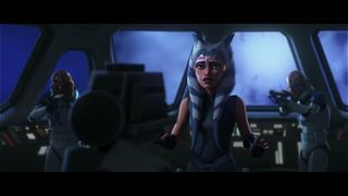 Still from Star Wars: The Clone Wars Season 7 Episode 11: Shattered. Ahsoka (orange skin, white face markings, white head tails with blue stripes) is in the cockpit of a Republic Cruiser spaceship. She is holding her hands up in a surrender-type motion. In the background you can see 2 clone troopers with orange helmets pointing guns at Ahsoka.