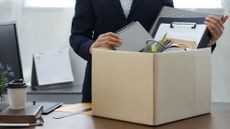 The torso of a businesswoman packing up her desk into a cardboard box, indicating she is leaving her post.