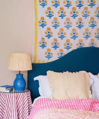 spring decorated bedroom with a blue headboard and a yellow block print floral wall hanging with pink and yellow bed linens and decor