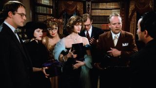 people in formal wear stand around a library in a still from Clue