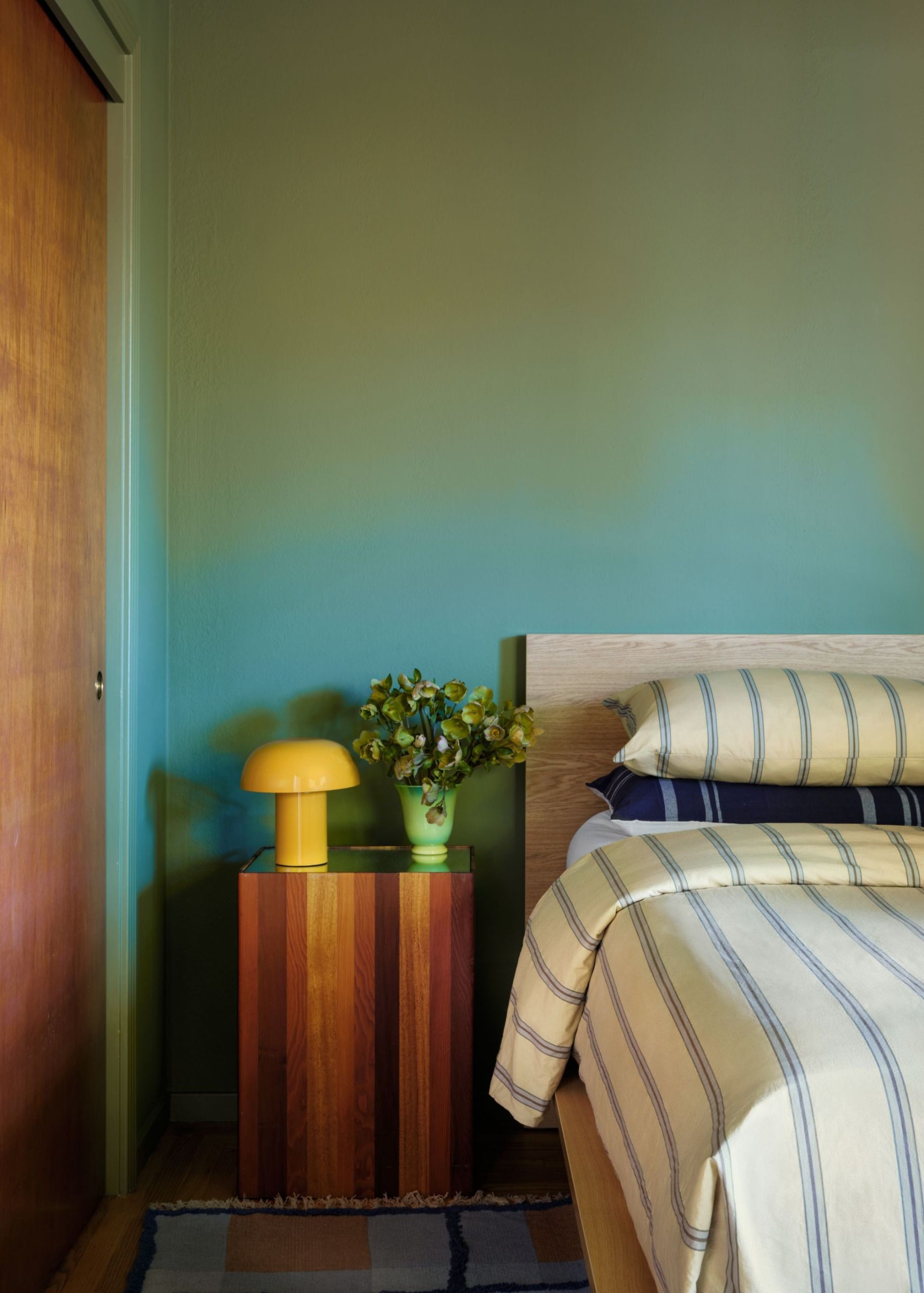 A bedroom with teal-toned walls, a blue bedspread and a bright yellow lamp