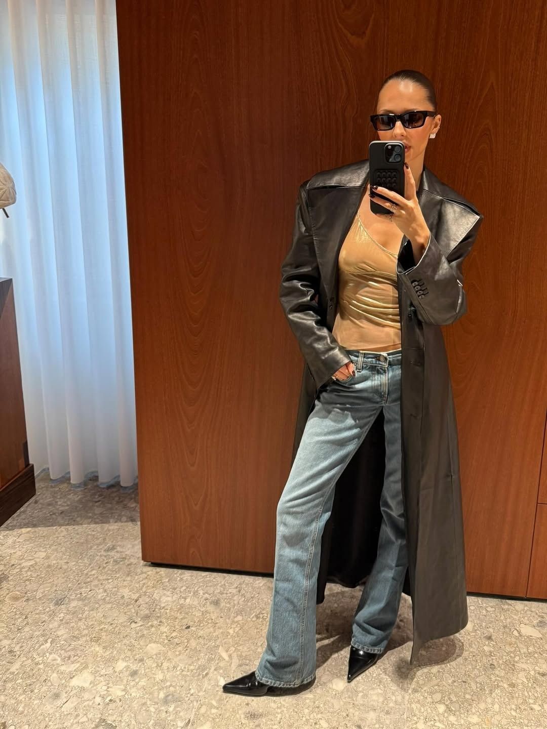 @piamance wears a pair of bootcut jeans, metallic top, and long leather trench.