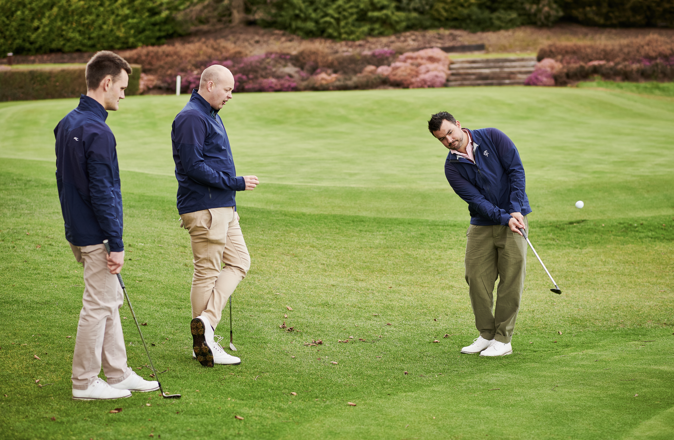 Golfer hits a chip shot watched on by his two playing partners