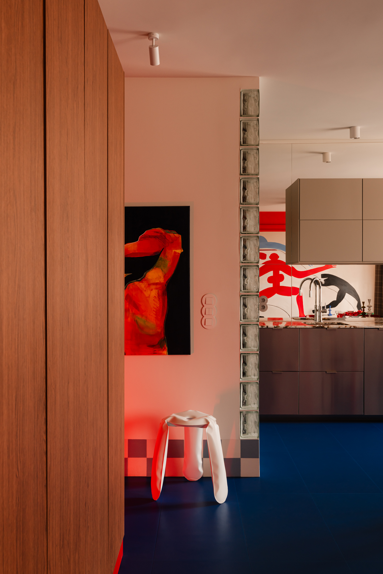 A view of an apartment with a bright blue floor, with a red accent light glowing from a hallway.