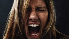 A young woman screaming uncontrollably while isolated on a black background