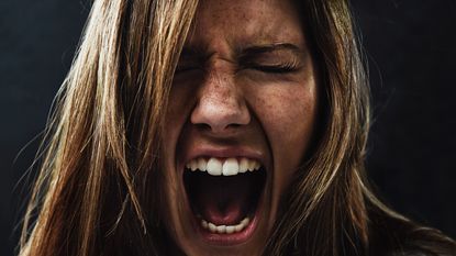 A young woman screaming uncontrollably while isolated on a black background