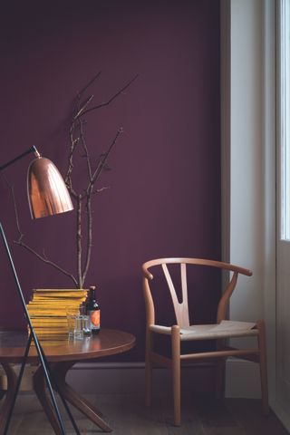 A living space with deep plum colored walls and a wooden chair in the window