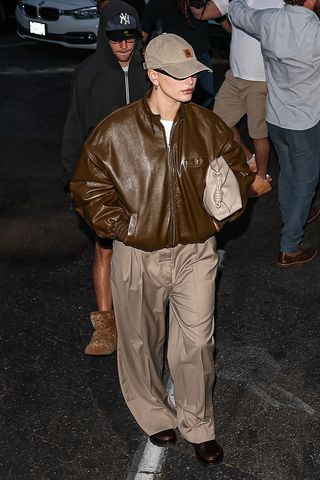 Hailey Bieber wearing a brown leather jacket and baseball cap