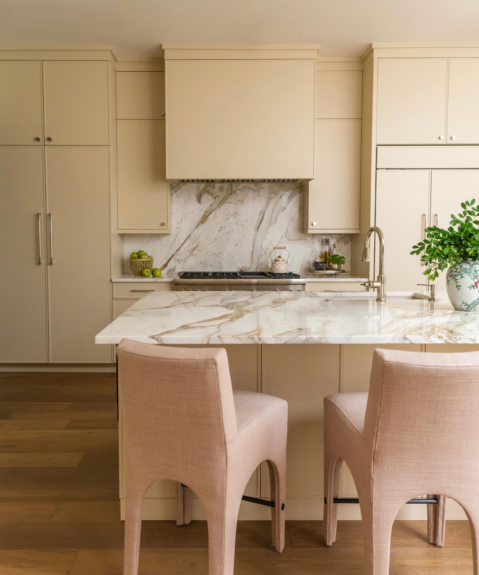 A warm neutral kitchen with marble countertops and pale pink upholstered bar stools