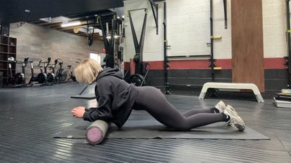 Woman in gym leaning elbows on a foam roller in modified plank position