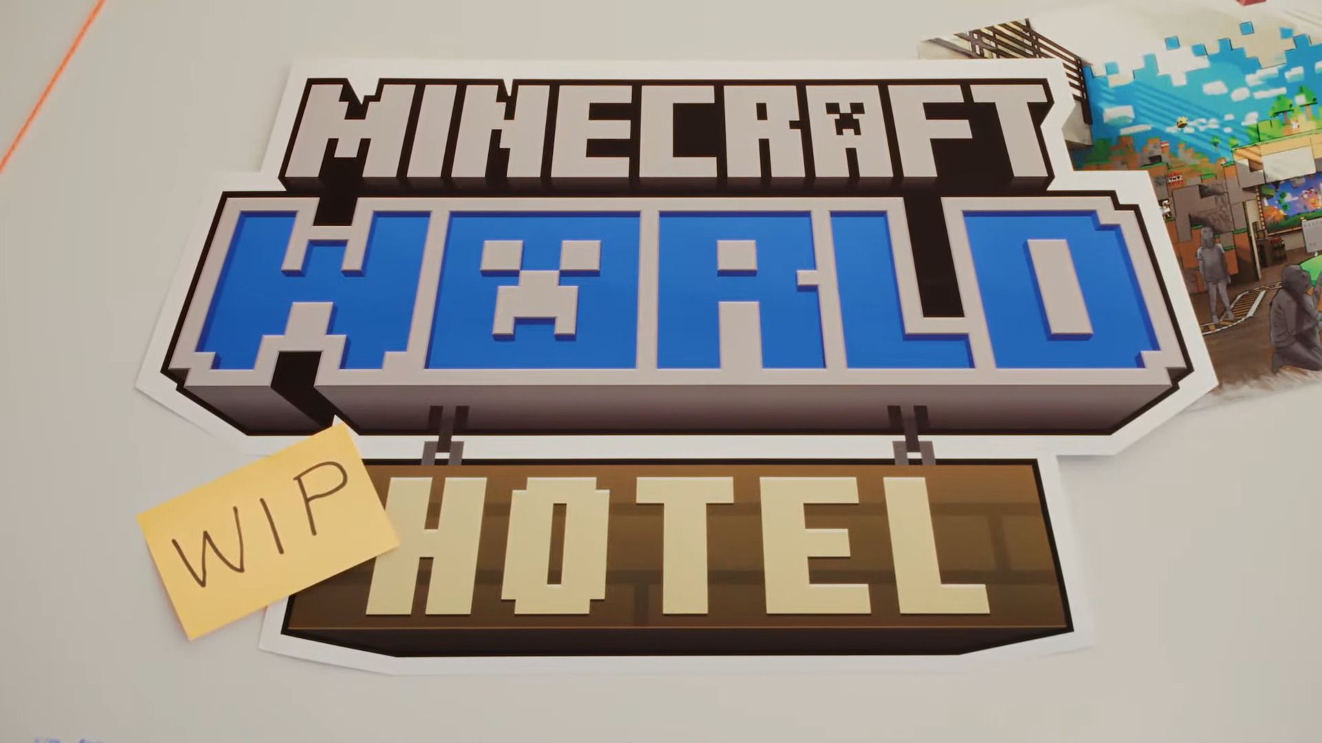 A sign featuring the Minecraft logo above a wooden hotel sign with a yellow sticky note labeled WIP attached to the left side on a white surface.