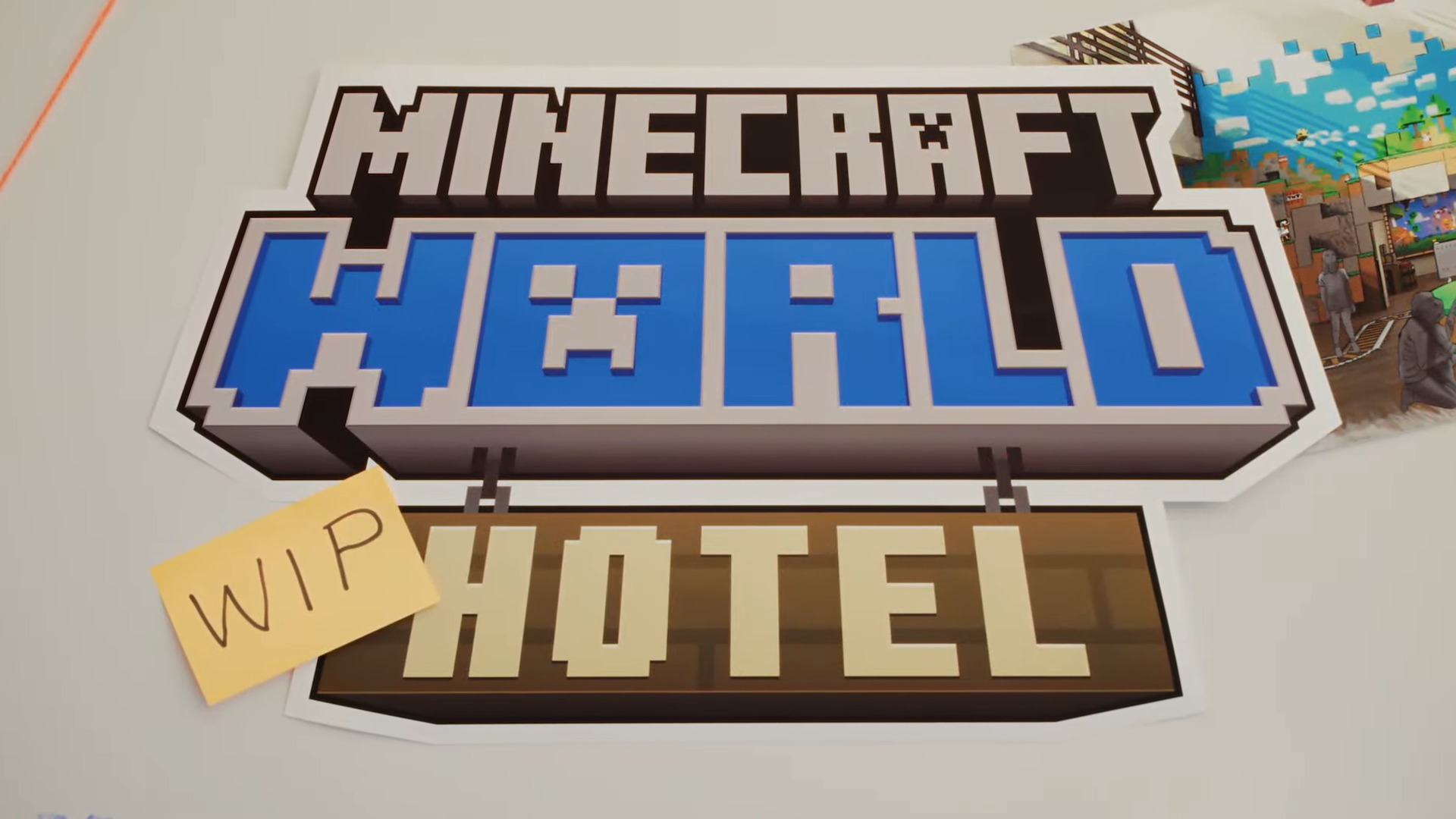 A sign featuring the Minecraft logo above a wooden hotel sign with a yellow sticky note labeled WIP attached to the left side on a white surface.