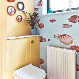 A toilet with a yellow-painted wall and a fish-print wallpaper covered wall