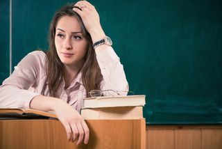 A teacher sits in her classroom looking exhausted