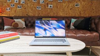 En HP EliteBook x360 1040 G8 står öppnad på ett ljust vardagsrumsbord med en vägg fylld med polaroidbilder i bakgrunden.