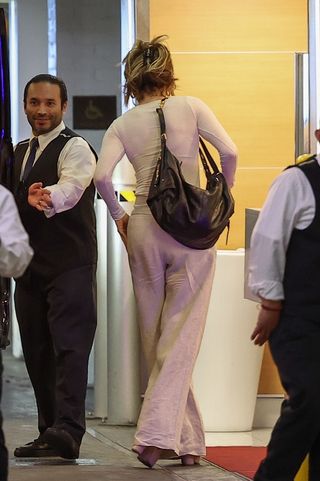 Jennifer Lopez walking into her office wearing khaki trousers and a white top with platform sandals and a designer bag