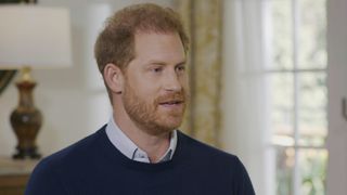 Prince Harry weating a white shirt under a navy jumper talking about his life in the Royal family 