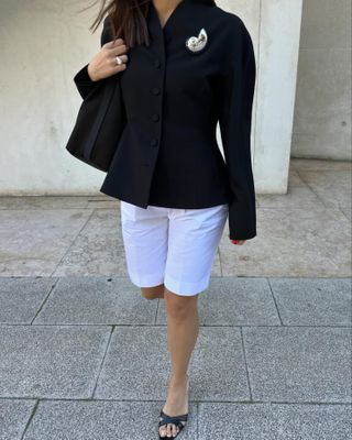 Woman in white Bermuda shorts, a blazer, and mules.