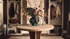 two hall trees with coats and boots on either side of an entryway with a round table in the middle styled with vases of flowers, dark paint, and a beige run