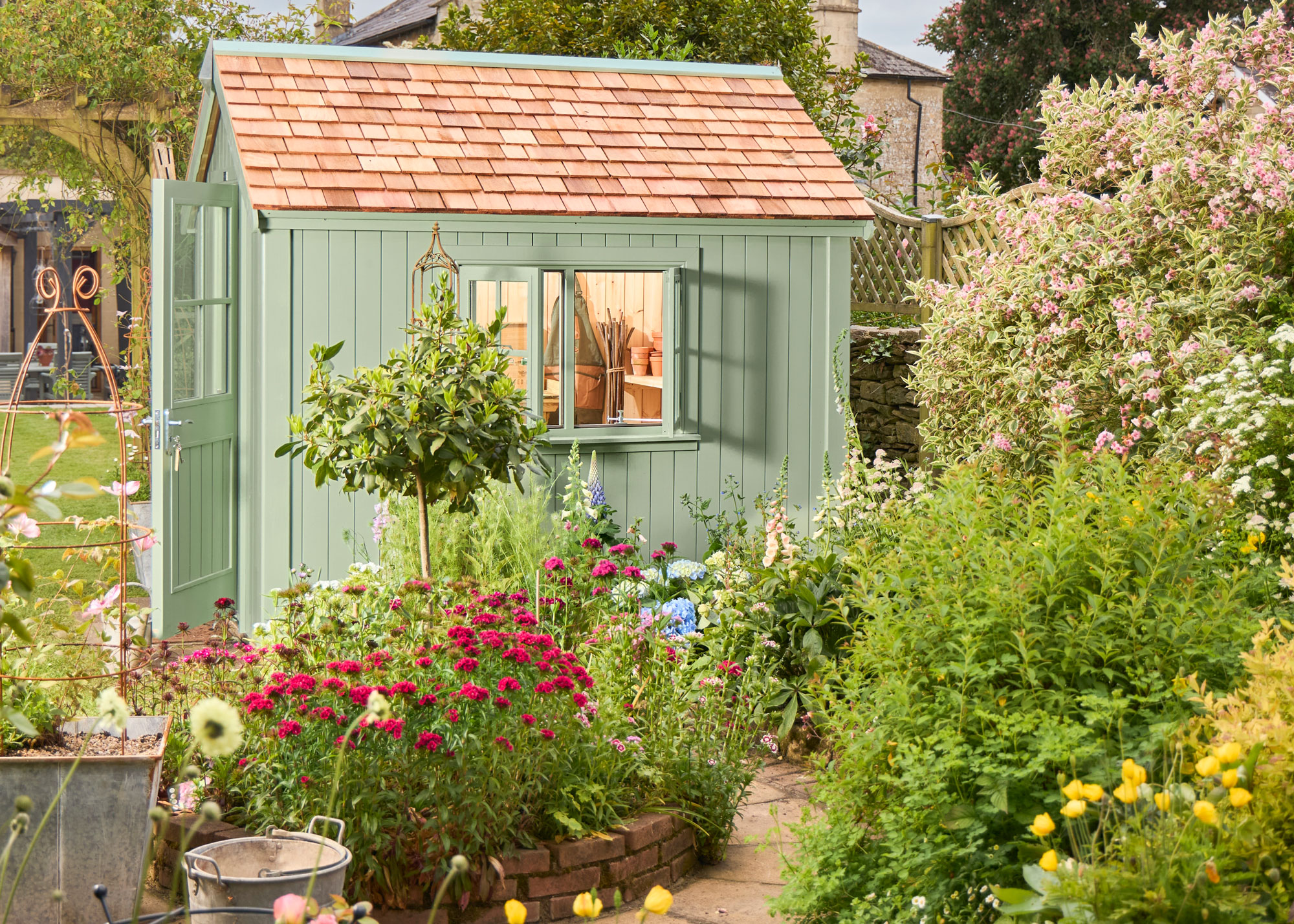 garden shed painted green with open door and windows, surrounded by planting and a garden path leading up to it