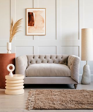 A chesterfield-style compact 2-seat Loveseat with grey wood-effect flooring, textured rug, wall paneling, statement floor lamp and side tables