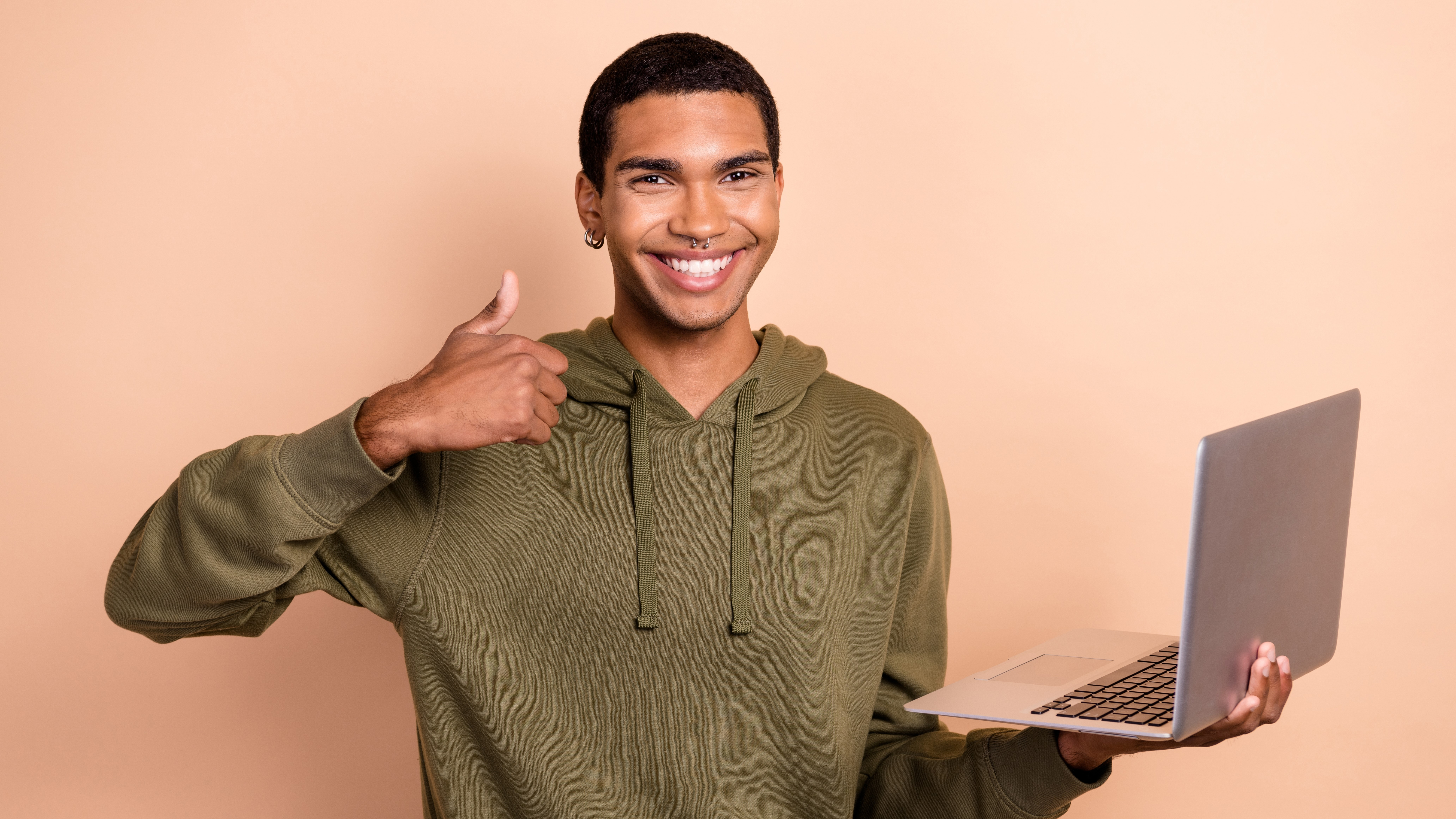 A cheerful man giving a thumbs-up while holding a MacBook.