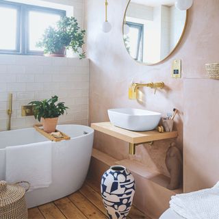 Modern bathroom with plaster walls, white sink, and white bath with wooden bath tray